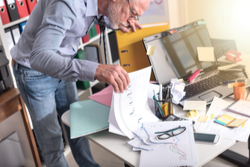 man looking through papers on cluttered home desk