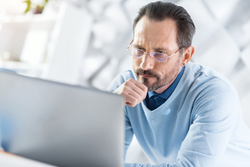 man in glasses looks at laptop