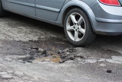 A car's wheel beside a road pothole